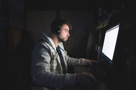 一个留着胡子戴着耳机的年轻人在晚上使用互联网晚上在图片