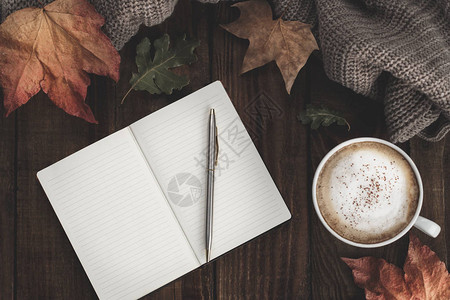 笔记本热咖啡卡布西诺毯子和秋叶等古老木质背景图片