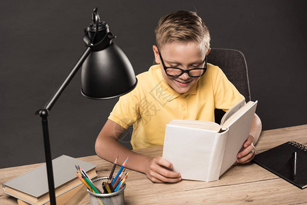 戴眼镜的男学生在桌上用彩色铅笔书籍教科书和灰色图片