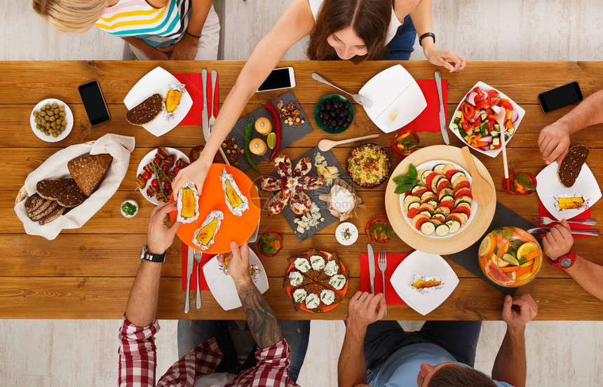人们在为聚会服务的节日餐桌上吃健康的饭菜朋友们在木桌顶视图上用有机食品庆祝女人把烤玉图片