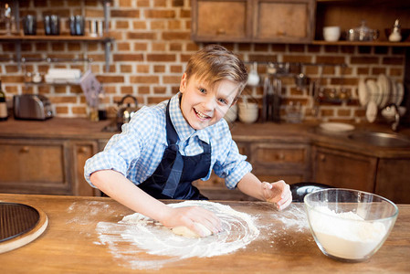 小男孩在厨房的木桌上做披萨面团背景图片