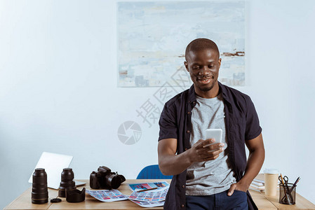 使用智能手机微笑的非洲裔美国摄影师的肖像图片