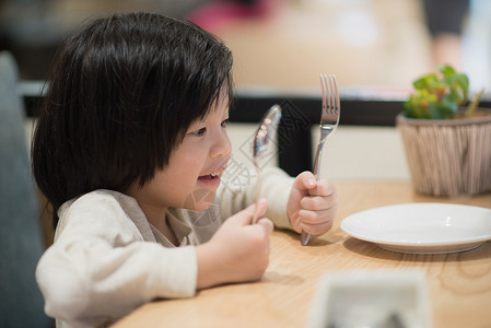亚洲可爱儿童在餐馆里拿着一勺子和图片