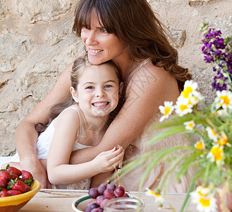 一位慈爱的母亲和年幼的女儿坐在户外度假屋餐桌旁吃新鲜水果图片
