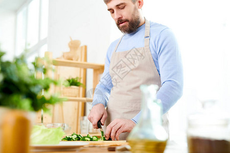 英俊成熟男子烹饪沙拉和在家宽敞的厨房里切菜的中段肖图片