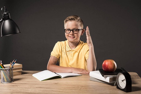 手举起手坐在桌边有钟表灯彩色铅笔书籍课本教科书和灰底苹图片