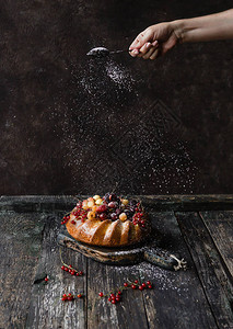 妇女用浆果在蛋糕上添加糖粉图片