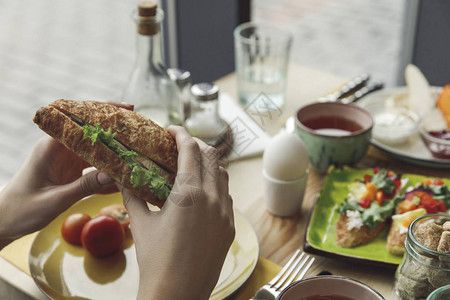 早餐时吃新鲜美味三明治的人图片