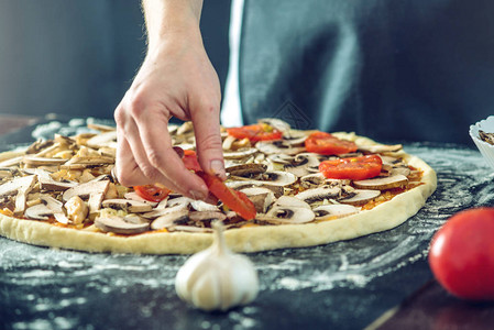穿黑围裙的厨师用手做比萨饼把披萨的原料放在桌子图片