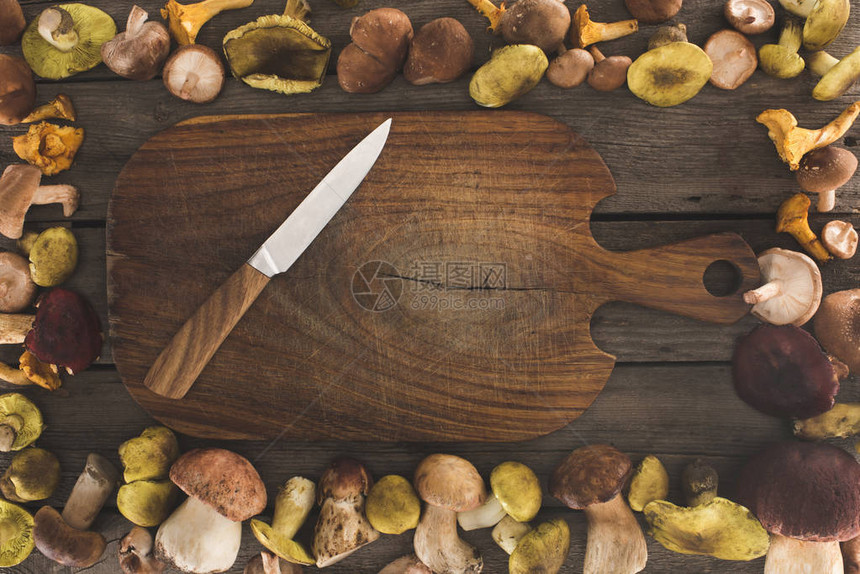 桌子上放着刀和蘑菇的木制切菜板的顶部视图图片