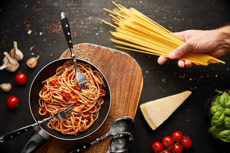人类将意大利面贴在美味的肉汤意面上在黑底煎锅里用新图片