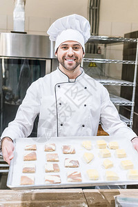 穿着厨师制服的面带微笑的面包师手持生背景图片