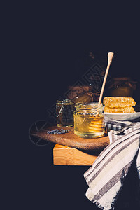 在黑背景餐桌上的剪切板上加蜂蜜的罐中蜜图片