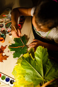 可爱的小女孩画秋天树叶坐在桌子图片
