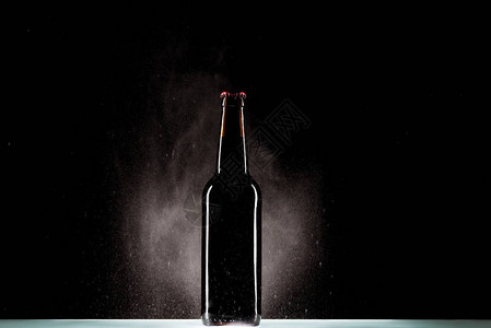 黑色背景上表面喷水的深色啤酒瓶背景图片