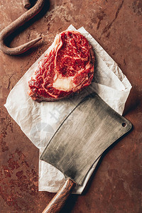 厨房桌面上生肉牛排金属钩和切肉刀的顶部视图图片