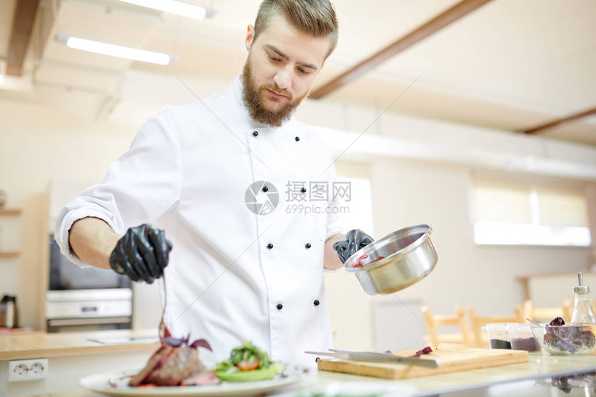 英俊专业厨师在现代餐厅厨房做饭时提供肉图片