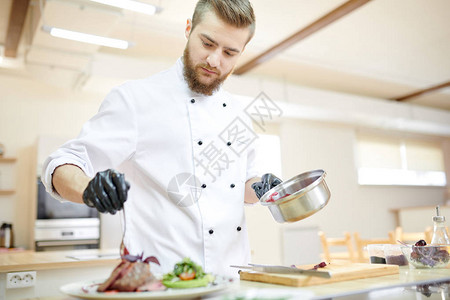 英俊专业厨师在现代餐厅厨房做饭时提供肉图片