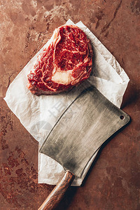 厨房桌面上生肉牛排烘焙纸和切肉刀的顶部视图图片