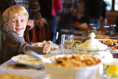 一个快乐的年轻孩子笑着坐在假日晚餐桌边拿着叉子盘坐图片