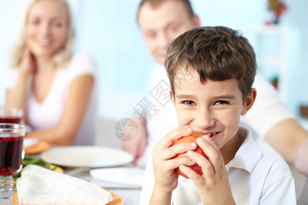 快乐男孩的肖像苹果坐在节庆桌边和他父母一起看相图片