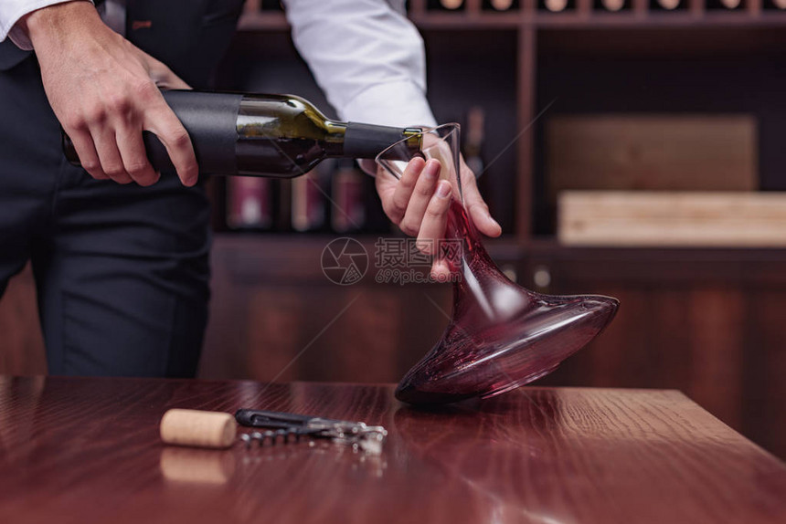 裁剪视图侍酒师将红酒从瓶中倒入酒窖中的酒瓶中图片