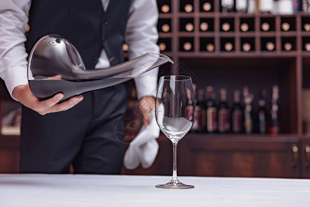裁剪视图侍酒师将红酒从醒酒器倒入酒窖餐桌上的玻璃杯中图片