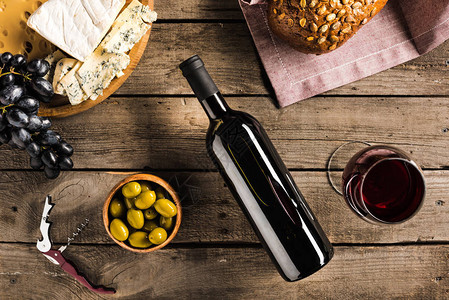 葡萄酒开瓶杯玻璃酒绿橄榄不同奶酪和木制桌顶图片