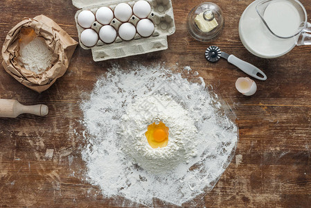 白面粉堆顶上看到木制桌上配有鸡蛋和烘烤成图片