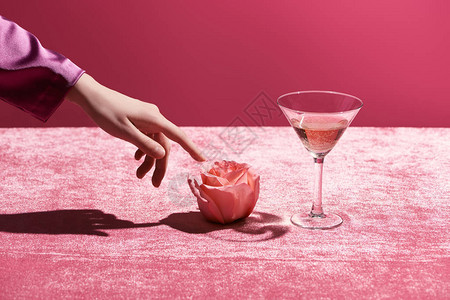妇女触碰靠近玻璃的玫瑰和在丝绒布上饮酒的妇女的作物风景背景图片