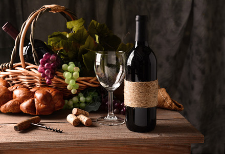 质朴的木桌上的葡萄酒静物与温暖的午后窗光一个老式的软木塞螺丝一篮葡萄和树叶一条面包和一些软木塞和一个空酒杯使图片