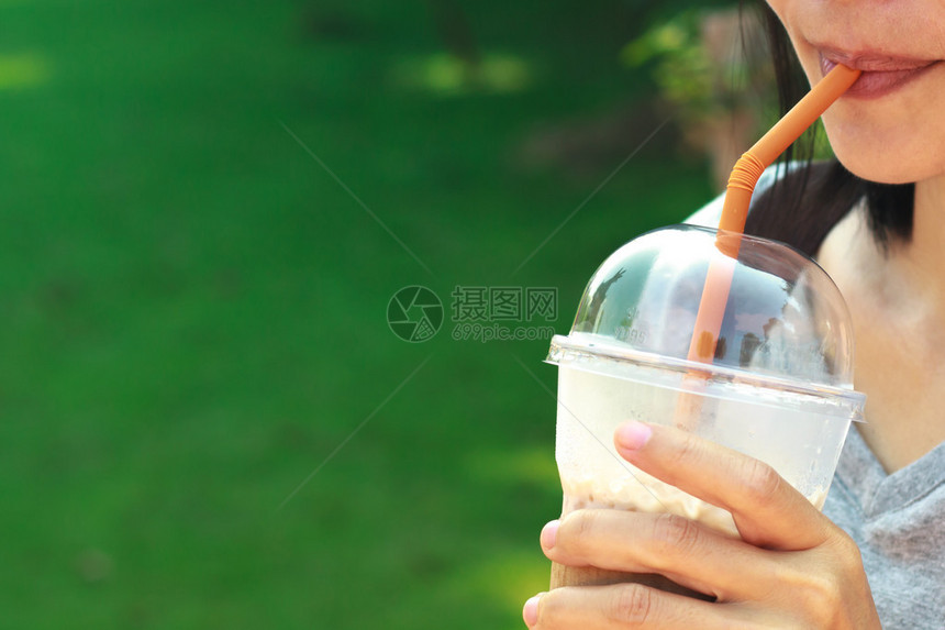 亚洲女在塑料玻璃杯中喝加牛奶的冰咖啡图片