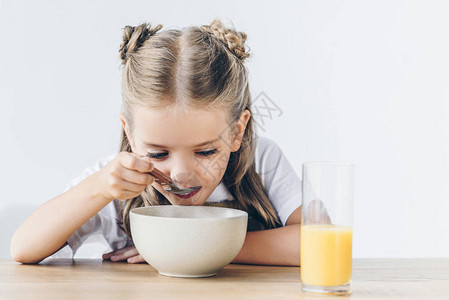 饥饿的小女学生在吃健康早餐时用白图片