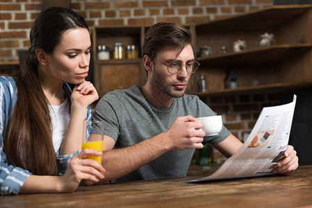 年轻女子在男子喝咖啡和阅读报纸图片