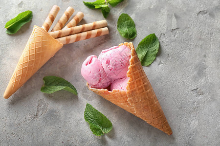 华夫蛋筒配美味的草莓冰淇淋和灰色背景的棍子图片