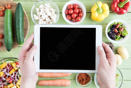 对持有数字平板电脑空白屏幕和木制桌上生蔬菜的人近视图片