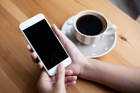 现代阁楼咖啡厅中手持白色手机空白黑屏和白咖啡杯的妇背景图片