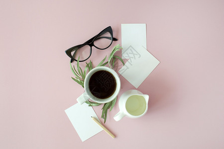 粉红背景的咖啡纸笔铅笔绿色叶子和眼镜图片