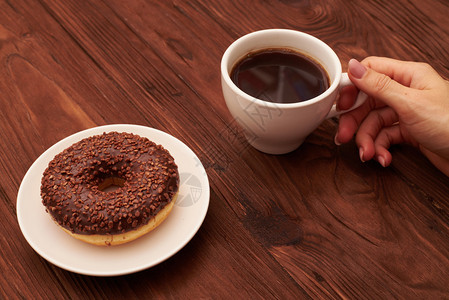 巧克力甜圈和女人手举着咖啡杯在棕图片