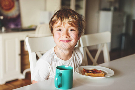 可爱的小男孩用果酱和热巧克力吃烤面包早餐时加果图片