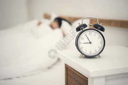 男人睡在卧室和闹钟的床上图片