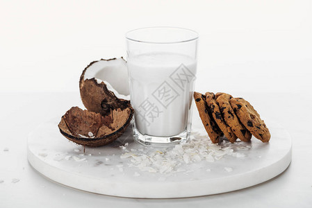 靠近椰子的玻璃杯中的椰子纯素牛奶和白色隔离图片
