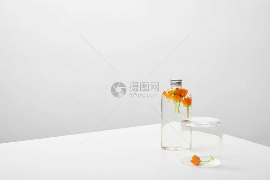 灰色背景的白色桌子上装有机美容产品和橙色野花的瓶子图片