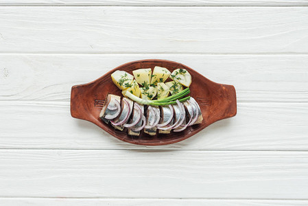 白色木质背景陶盘中用土豆和洋葱腌制鲱图片