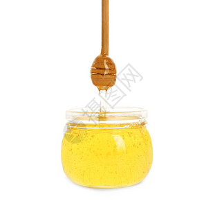 蜂蜜从白色背景的罐子里的勺子滴下来图片