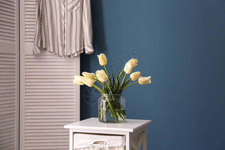 桌上有美丽郁金香的花瓶靠在彩色墙上图片