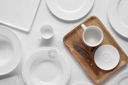 白桌上的杯子不同盘子木托盘碗和叉子的顶视图图片