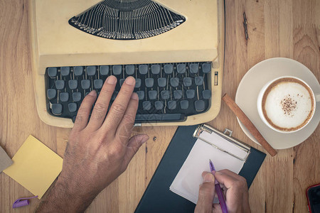 在木桌上使用老式打字机和一杯咖啡的人图片