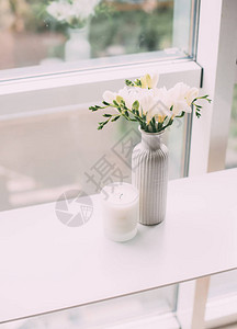 窗边桌上的花瓶和芳香蜡烛中的白色自由白布束图片