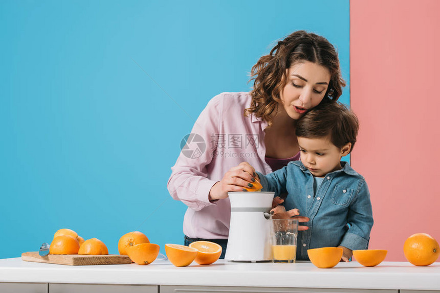 可爱的小可爱男孩妈挤压新鲜橙汁在果汁机图片